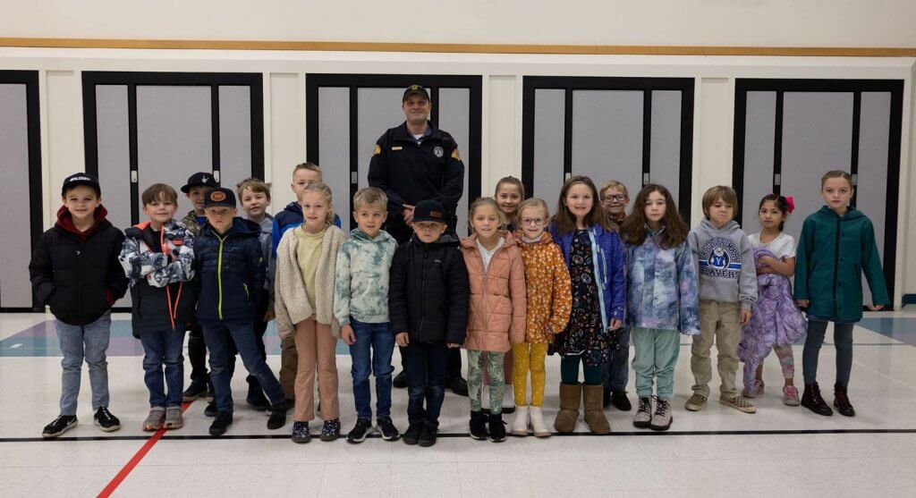 A state patrol sargent stands with a group of 2nd graders in a gym facing the camera